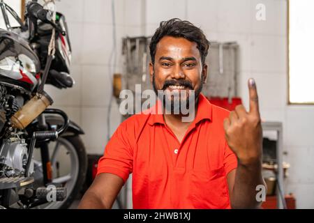 joyeux mécanicien souriant montrant l'encre marquée du doigt de l'électeur après avoir fait le vote à l'élection - concept de responsabilité, de démocratie et de droite Banque D'Images