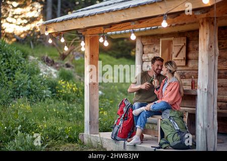 Un jeune couple qui a bavardé et avoir un verre au porche du chalet dans la forêt lors d'une belle journée. Vacances, nature, chalet, relation Banque D'Images