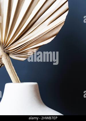 Vase rond élégant en céramique avec feuilles de palmier séchées. Arrière-plan bleu foncé. Vue avant. Copier l'espace Banque D'Images