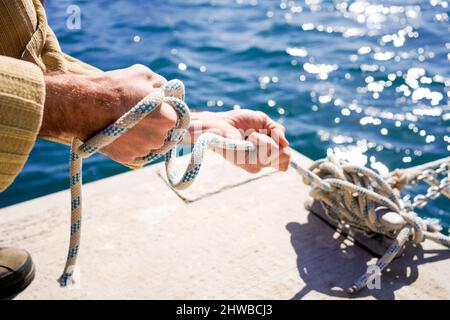 des mains fortes d'un marin accroupi nouant des cordes de navire et nouant des nœuds sur le quai d'amarrage d'un port Banque D'Images