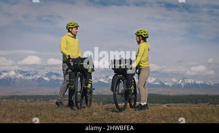 L'homme et la femme voyagent sur un terrain mixte en vélo avec bikepacking. Les deux personnes voyage avec des sacs de vélo. Sport bikepacking, vélo, vêtements de sport dans les couleurs vert noir. Montagne enneigée. Banque D'Images