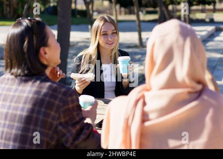 Trois filles diverses ayant la pause-café et bavardant dans le parc de la ville Banque D'Images