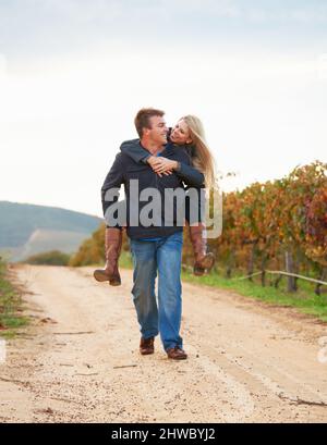 S'amuser tout en se moquant. Un jeune homme portant sa petite amie sur son dos tout en marchant sur un vignoble. Banque D'Images