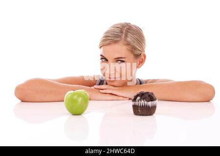 Un choix aussi difficile. Une jolie jeune femme qui fait le choix entre un cupcake ou une pomme. Banque D'Images