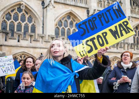 Bath, Royaume-Uni. 5th mars 2022. Une femme drapée dans le drapeau ukrainien tient un écriteau anti-Poutine / stop à la guerre alors qu'elle écoute les discours devant l'abbaye de Bath lors d'une manifestation contre l'invasion de l'Ukraine par la Russie. La manifestation a été organisée afin de permettre aux populations locales de manifester leur solidarité avec l'Ukraine dans la guerre Russie-Ukraine et de condamner les actions de Poutine. Credit: Lynchpics/Alamy Live News Banque D'Images