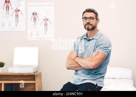 Vous aider à guérir est mon travail. Portrait d'un beau kinésithérapeute mature de sexe masculin posant avec ses bras pliés dans son bureau. Banque D'Images