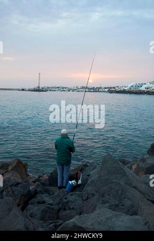 homme pêchant au large des rochers de la mer au coucher du soleil playa blanca lanzarote îles canaries espagne Banque D'Images
