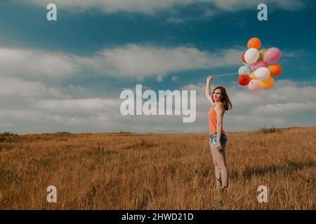 Belle jeune femme marchant sur un pré tenant des ballons Banque D'Images