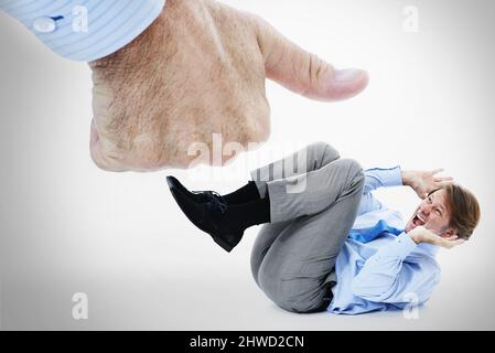 Peur du succès. Photo studio d'un homme d'affaires effrayé se protégeant d'un pouce géant. Banque D'Images