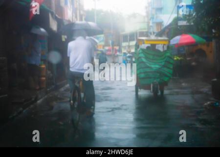 Image floue de Howrah, Bengale-Occidental, Inde. Personnes à vélo et conduite d'un minibus sur la rue humide avec des parasols, image de mousson prise par la fenêtre de voiture Banque D'Images