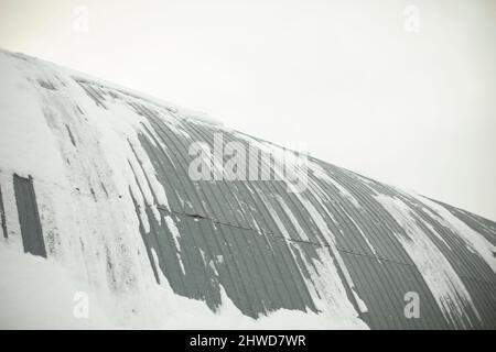 L'entrepôt est dans la neige. Paroi en acier. La neige roule sur le toit. Surface nervurée. Banque D'Images