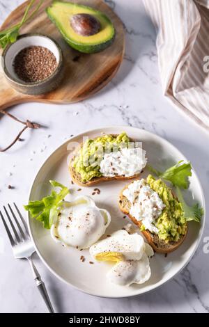 Petit-déjeuner ou brunch de Pâques. Délicieux petit déjeuner ou en-cas - œufs pochés et fromage à la crème pain de seigle complet, avocat sur un plan d'examen en marbre. Banque D'Images