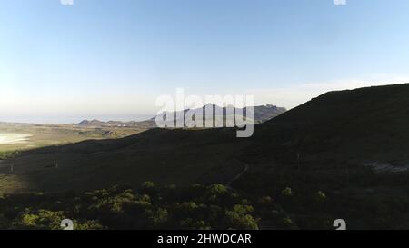 Vue aérienne de la petite colonie dans les collines vertes avec chaîne de haute montagne et mer bleue sur le fond bleu ciel. Magnifique paysage coloré Banque D'Images