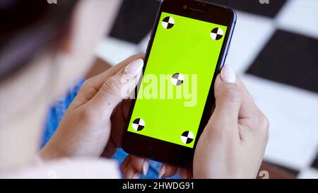 Gros plan d'une femme regardant dans le téléphone avec écran vert. Films. Belle jeune femme fixe avec attention dans le téléphone avec écran vert à insérer. Banque D'Images