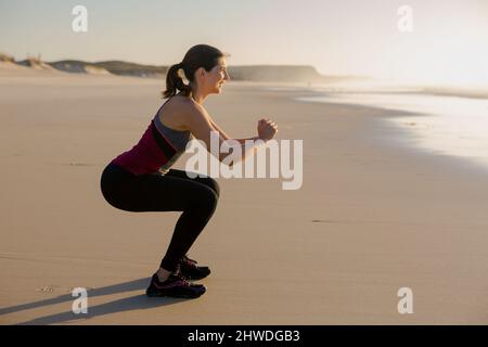 Tirer d'une belle femme qui s'accroupit dans la plage d'exercices Banque D'Images