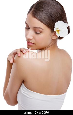 Shes a une peau magnifique. Studio photo d'une belle jeune femme avec une orchidée dans ses cheveux regardant au-dessus de son épaule. Banque D'Images