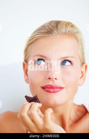 MMM, c'est céleste. Jeune femme souriante appréciant un délicieux morceau de chocolat. Banque D'Images