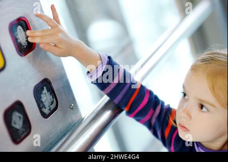 Jolie petite fille appuyant sur le bouton de l'ascenseur avec son doigt. Enfant qui atteint un bouton dans un ascenseur. Banque D'Images