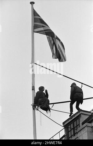 Deux hommes en kit de mountaineers ont grimpé le mât sur la Rhodésie House à minuit le 11th janvier - ils ont descendu le drapeau de Rhodésie, l'ont remplacé par l'Union Jack et ont dit aux policiers qui ont essayé des descendre, Ils restaient mis jusqu'à la manifestation de l'après-midi le 12th janvier à l'extérieur de la maison de Rhodésie. A 10am ans, ils avaient des sandwiches alors qu'ils étaient encore sur le mât et ensuite l'un d'eux a lu un livre. 12th janvier 1969. Banque D'Images