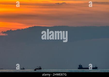 Cargo et bateaux de pêche devant le coucher du soleil sur les toilettes. Vue vers l'ouest depuis la côte de Norfolk. Banque D'Images