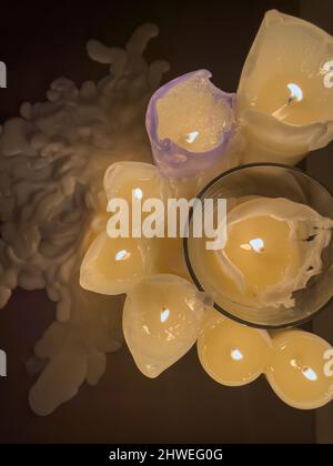 plusieurs bougies allumées se tiennent sur une table dans un intérieur sombre, la cire fondue autour des bougies, vue à angle élevé Banque D'Images