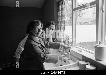 Le comédien Ken Dodd ouvre des appartements à Ducie Street et Beaconsfield Street, Toxteth, Liverpool. Deux maisons, une dans chaque rue, ont été converties en appartements sous la direction d'une équipe d'experts en logement et en planification. Ken boit une tasse d'eau dans la nouvelle cuisine de Mme Margaret Gibbs, rue Ducie. 7th avril 1970. Banque D'Images