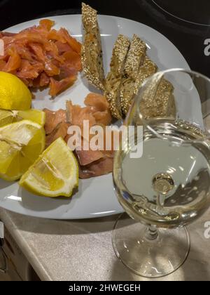 Une vie romantique avec un verre de vin blanc sur la table, une assiette de poisson rouge salé et fumé, des tranches de citron et du pain Banque D'Images