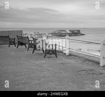 Photo en noir et blanc des bancs en bois sur le toit de la falaise Cromer surplombant la plage et la célèbre jetée de l'époque victorienne. Banque D'Images