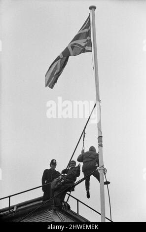 Deux hommes en kit de mountaineers ont grimpé le mât sur la Rhodésie House à minuit le 11th janvier - ils ont descendu le drapeau de Rhodésie, l'ont remplacé par l'Union Jack et ont dit aux policiers qui ont essayé des descendre, Ils restaient mis jusqu'à la manifestation de l'après-midi le 12th janvier à l'extérieur de la maison de Rhodésie. A 10am ans, ils avaient des sandwiches alors qu'ils étaient encore sur le mât et ensuite l'un d'eux a lu un livre. 12th janvier 1969. Banque D'Images