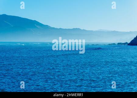 Scène à travers la baie de Tokomaru aux collines tandis que le soleil se couche et met en évidence la mer brume au-dessous des collines lointaines. Banque D'Images