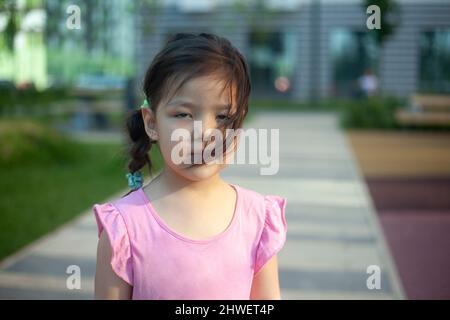 Portrait de l'enfant dans la rue. Fille d'apparence asiatique. L'enfant se trouve sur le sentier. Marchez en été dans la cour de la maison. Poils du visage à l'avant-chooler Banque D'Images