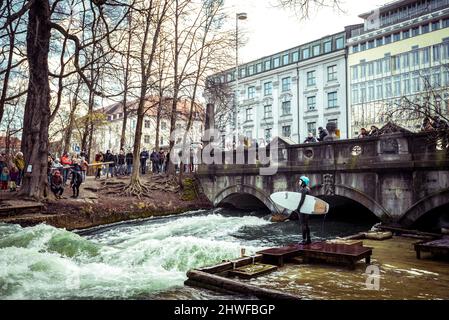 Munich, Allemagne, 27.02.2022: Surf d'hiver sur la rivière le jour ensoleillé sur Eisbach Wave à Munich, Bavière, Allemagne. Banque D'Images