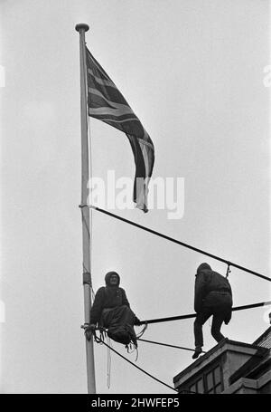 Deux hommes en kit de mountaineers ont grimpé le mât sur la Rhodésie House à minuit le 11th janvier - ils ont descendu le drapeau de Rhodésie, l'ont remplacé par l'Union Jack et ont dit aux policiers qui ont essayé des descendre, Ils restaient mis jusqu'à la manifestation de l'après-midi le 12th janvier à l'extérieur de la maison de Rhodésie. A 10am ans, ils avaient des sandwiches alors qu'ils étaient encore sur le mât et ensuite l'un d'eux a lu un livre. 12th janvier 1969. Banque D'Images