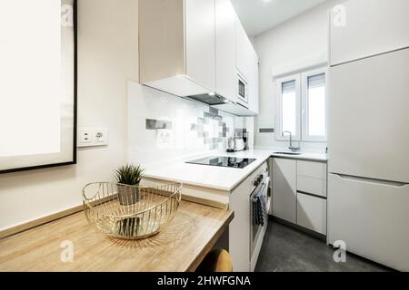 Armoires de cuisine disposées en L sur les murs blancs de la chambre avec des appareils blancs et une petite table de petit-déjeuner en chêne Banque D'Images