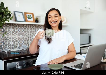 Je ne peux pas commencer sans café. Portrait d'une jeune femme qui boit du café tout en travaillant sur un ordinateur portable à la maison. Banque D'Images