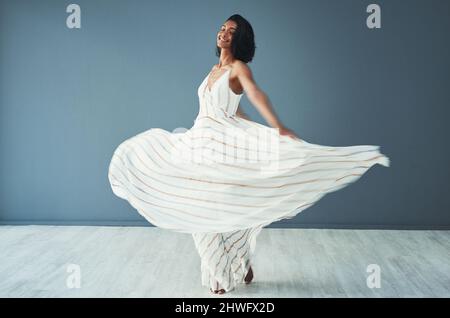 Ce que vous portez doit vous faire sentir libre et confortable. Photo d'une belle jeune femme portant une longue robe évasée sur fond bleu. Banque D'Images