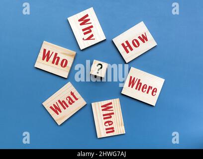 5 questions WS et 1 H sur cube en bois sur fond bleu dont les réponses sont essentielles pour résoudre les problèmes. Banque D'Images