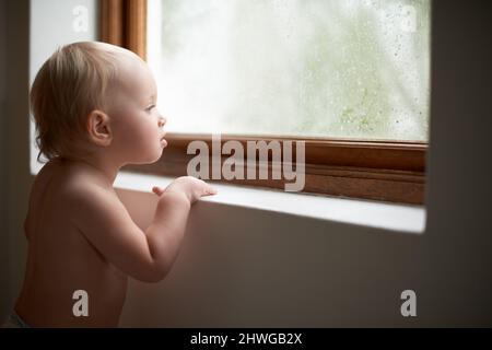 Curieux jeune esprit. Une petite fille regardant par la fenêtre. Banque D'Images