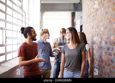 Rattraper le retard sur le chemin de la classe. Photo d'un groupe diversifié d'amis universitaires parlant dans un couloir. Banque D'Images