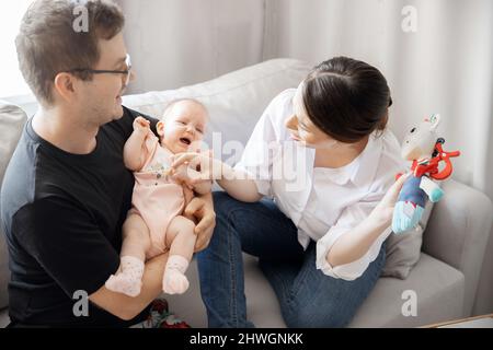 Les jeunes parents, le père et la mère, essaient de calmer les pleurs et l'inquiétude de la petite fille à la maison. Concept parental. Banque D'Images