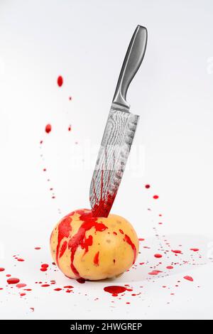 Thème étrange montrant une pomme de terre crue poignardée avec un couteau de cuisine soudé à motif dans le dos sanglant de lumière Banque D'Images