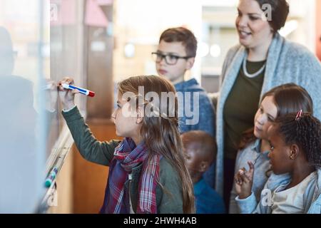 Continuez, vous faites un excellent travail. Photo rognée d'une jeune fille de l'école élémentaire qui écrit sur un tableau blanc dans la salle de classe. Banque D'Images