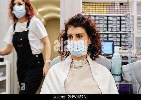 Femme portant un masque facial assis dans une chaise au salon de coiffure. Banque D'Images