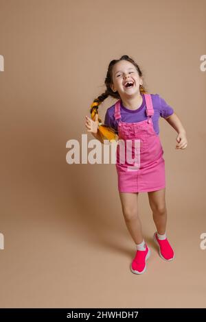 Une femme heureuse et rayonnante qui s'amuse avec deux queues de cochon kanekalon de couleur jaune vêtues d'une combinaison rose, d'un t-shirt violet et d'un rose Banque D'Images