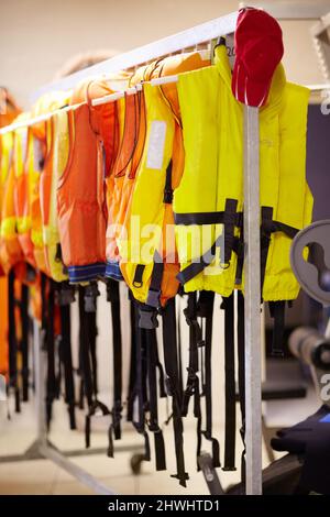 Prêt au besoin. Coupe courte de gilets de sauvetage suspendus sur un rail à l'intérieur d'un poste de maître-nageur. Banque D'Images