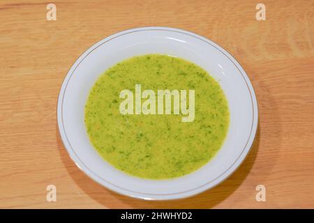 Soupe verte biologique saine servie dans une assiette avec le bord doré sur la table naturelle en bois, idéale pour le déjeuner Banque D'Images