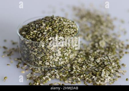 Diviser les lentilles de haricots moong dans un petit bol en verre. Tourné sur fond blanc avec pile de grains de moong fendus sont dispersés autour. Banque D'Images