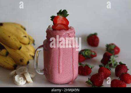 Smoothie fait de fraises fraîches, de banane et de lait d'amande. Servi dans un pot de maçon. Tourné sur fond blanc avec des bananes et des fraises. Banque D'Images