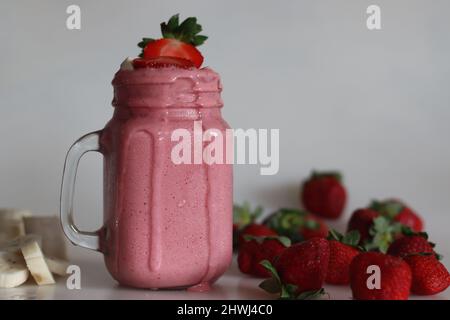 Smoothie fait de fraises fraîches, de banane et de lait d'amande. Servi dans un pot de maçon. Tourné sur fond blanc avec des bananes et des fraises. Banque D'Images