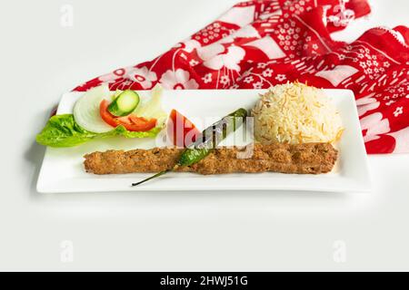 Style turc, l'adana kebab avec du riz et de la salade dans un plat isolé sur une nappe colorée vue latérale sur fond gris Banque D'Images